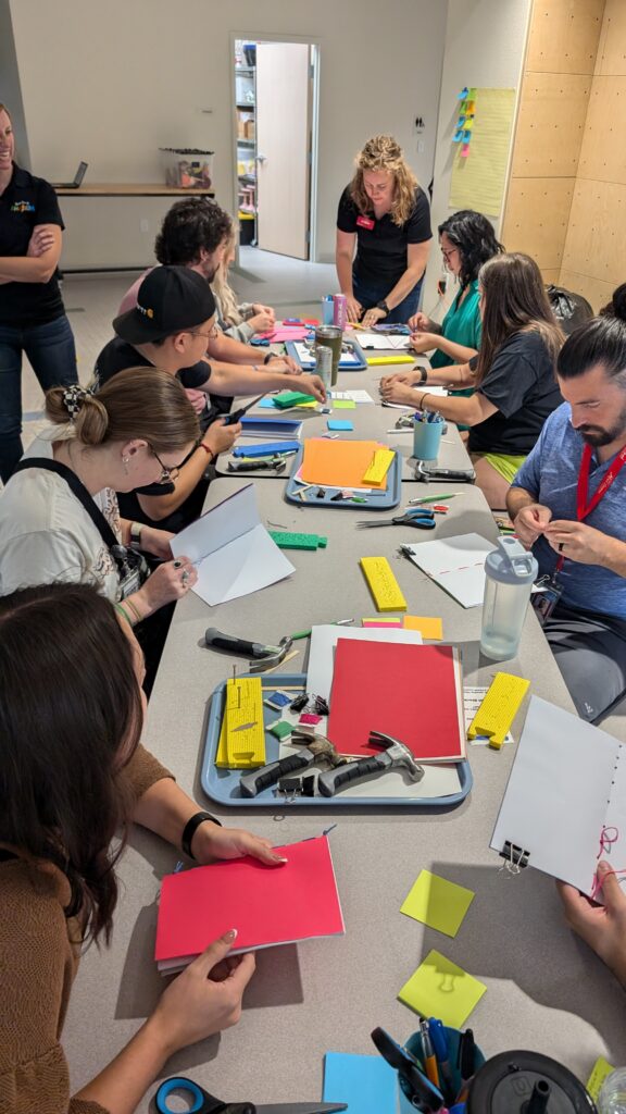 A group of people sit around a table making handmade notebooks